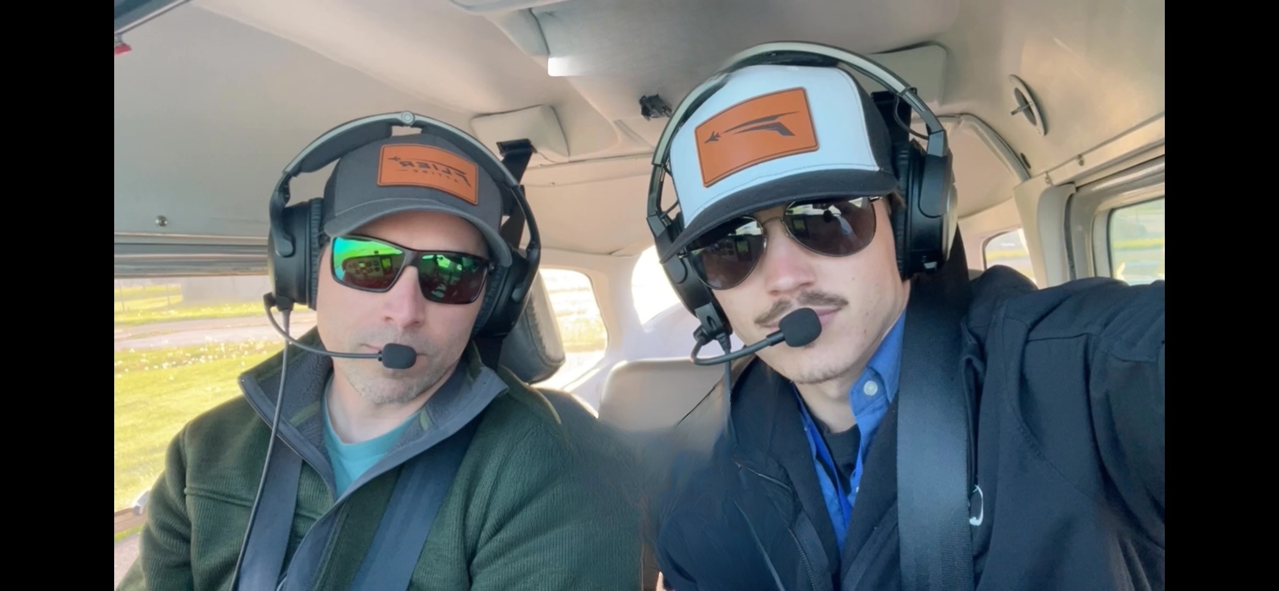 Founder Mark Rolfes in the cockpit with a flight student, both wearing Flier Attire hats