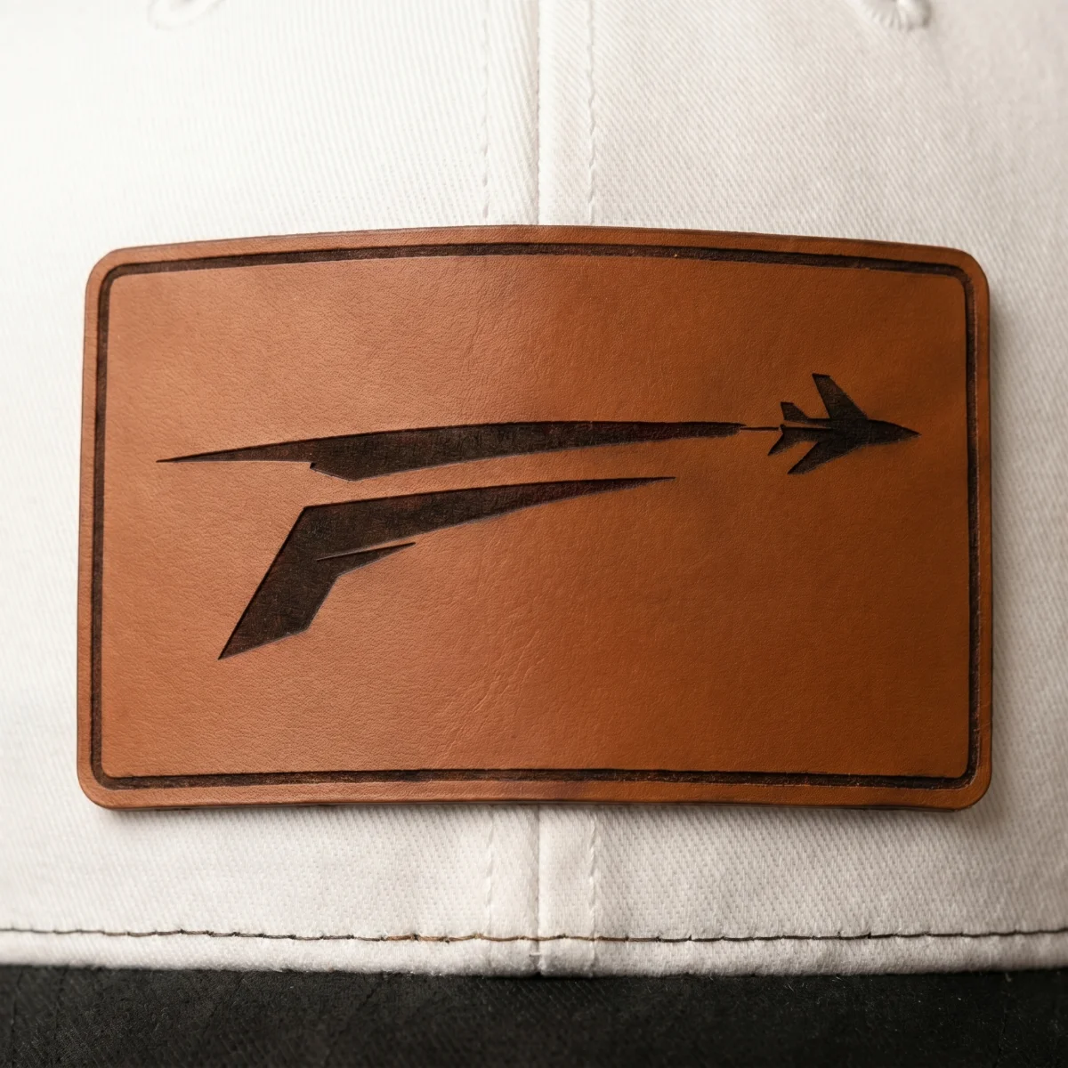 Cognac leather patch on The Icon with engraved F and jet mark, centered on white front panel