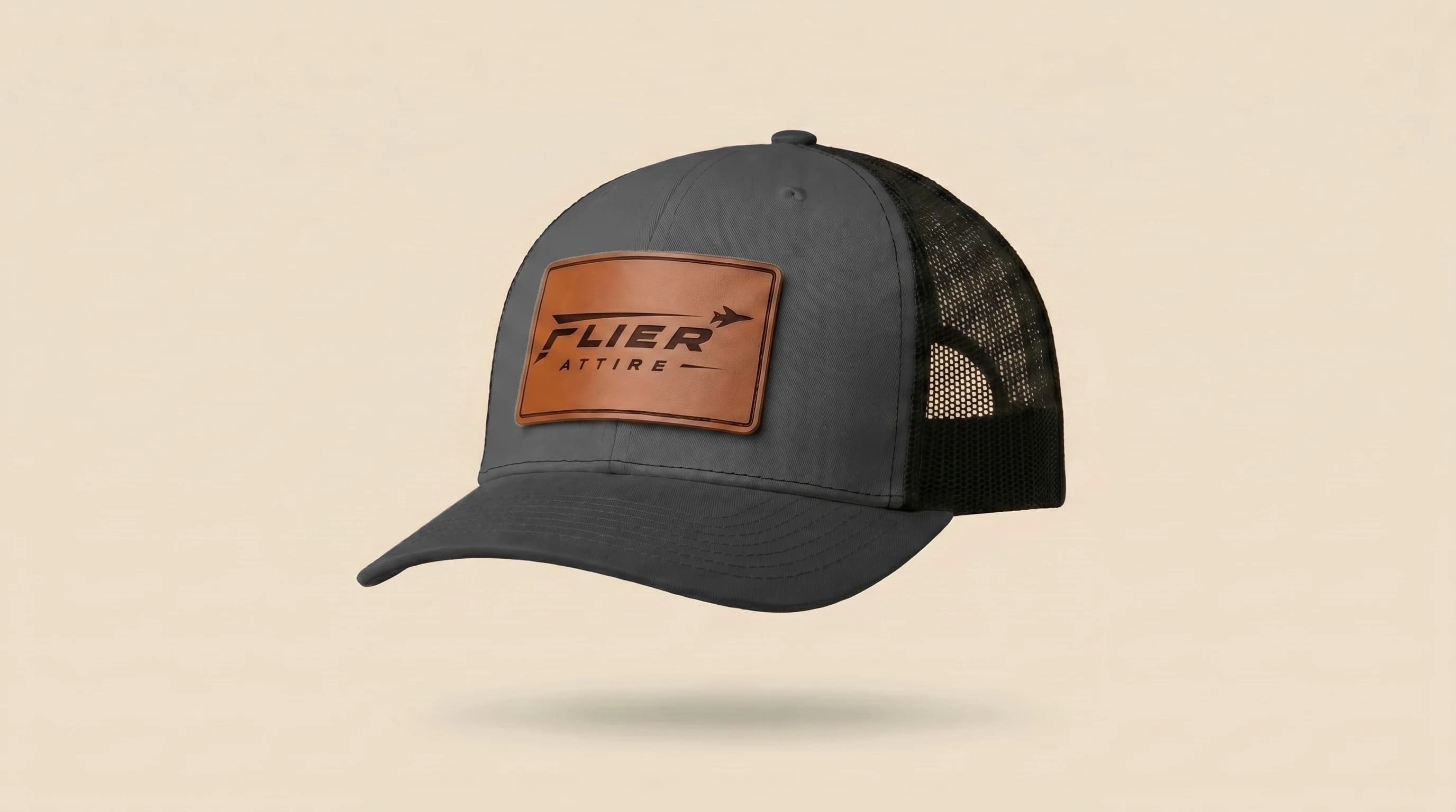 The Signature trucker hat, three-quarter view. Grey crown, grey bill, cognac leather patch with full Flier Attire wordmark.